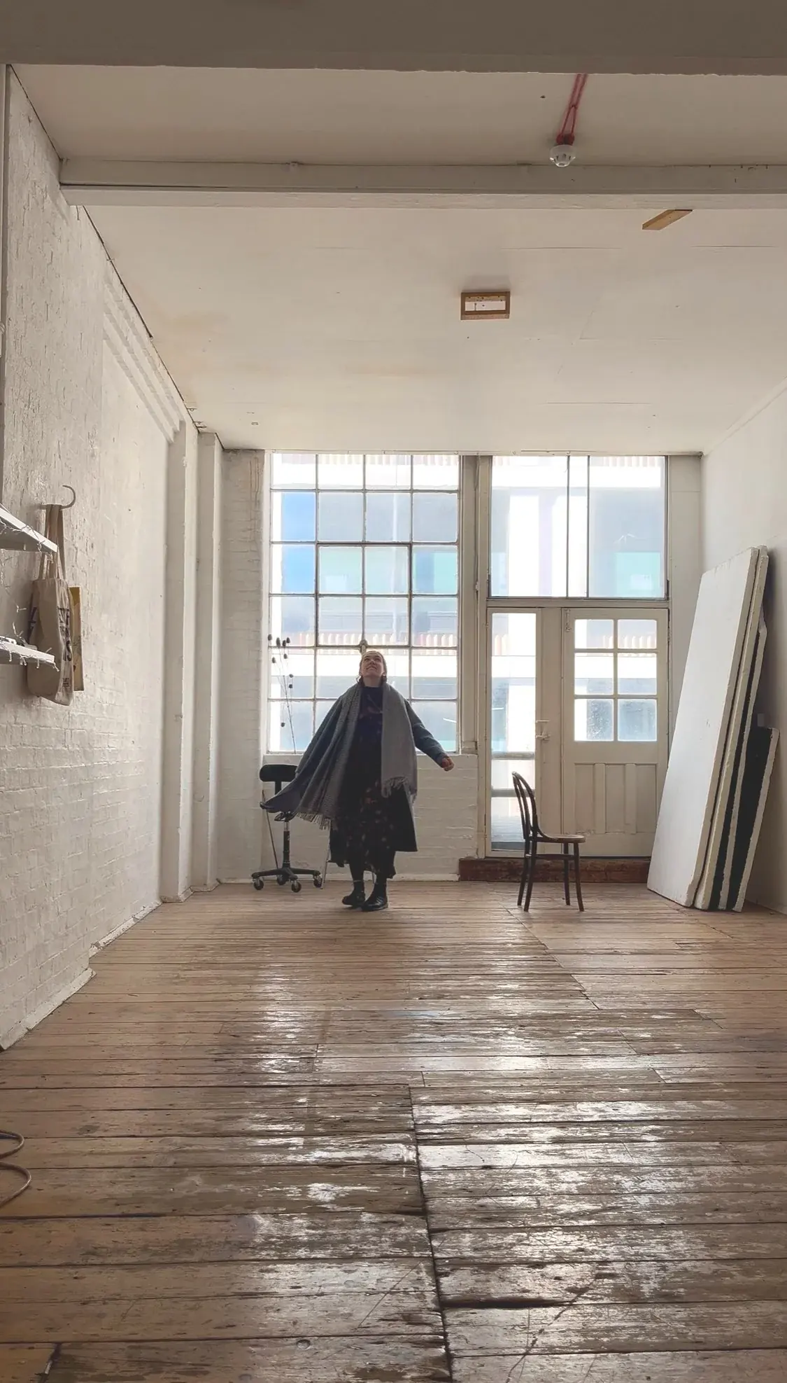 The empty Angel studio before it opened: a bright room with a wooden floor, tall windows and white brick walls, with a person in a grey shawl standing in the middle looking up