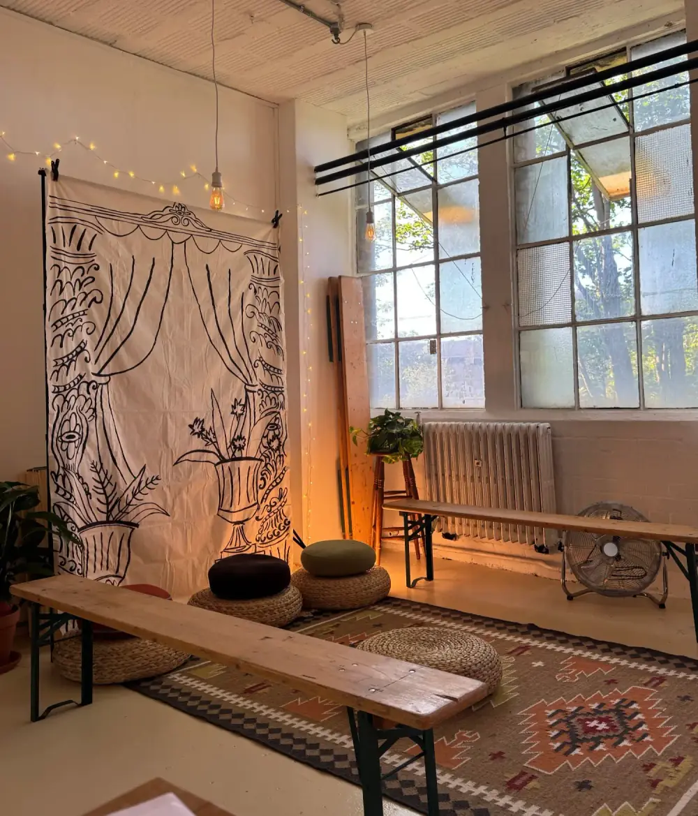 The Cosy Corner at Peckham: floor cushions on a patterned rug, a hand-painted theatre curtain backdrop, fairy lights and tall studio windows